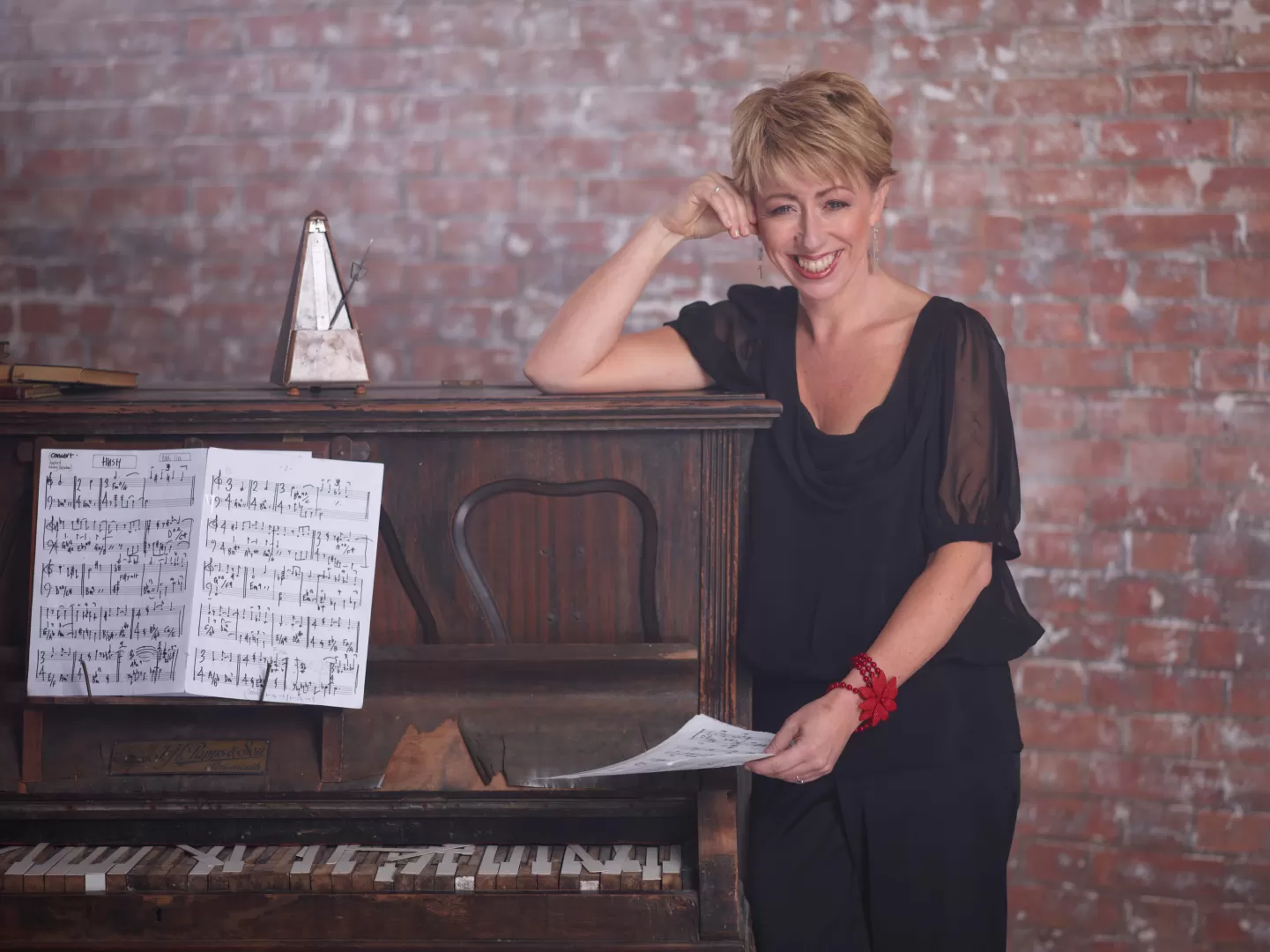 Porträt von Nikki Iles, sie steht neben einem Klavier und hält ein Notenblatt in der Hand.
