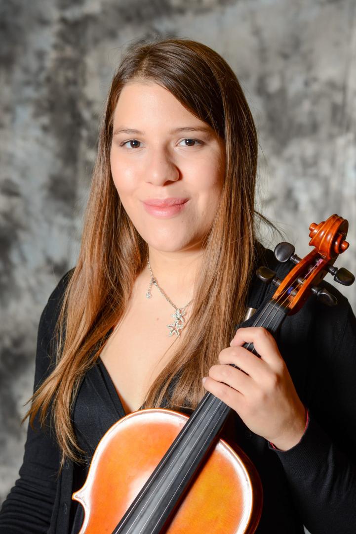 Elena Solórzano sitzt vor einem grauen Hintergrund, hält ihre Viola in der Hand und lächelt in die Kamera. Sie hat lange, braune Haare und braune Augen. Sie trägt schwarze Kleidung und eine silberne Kette mit zwei Sternen.