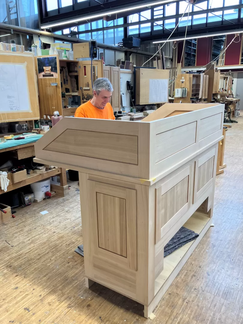 Ein Mitarbeiter in einem orangenen T-Shirt steht hinter dem Spieltisch-Gehäuse inmitten der Werkstatt.