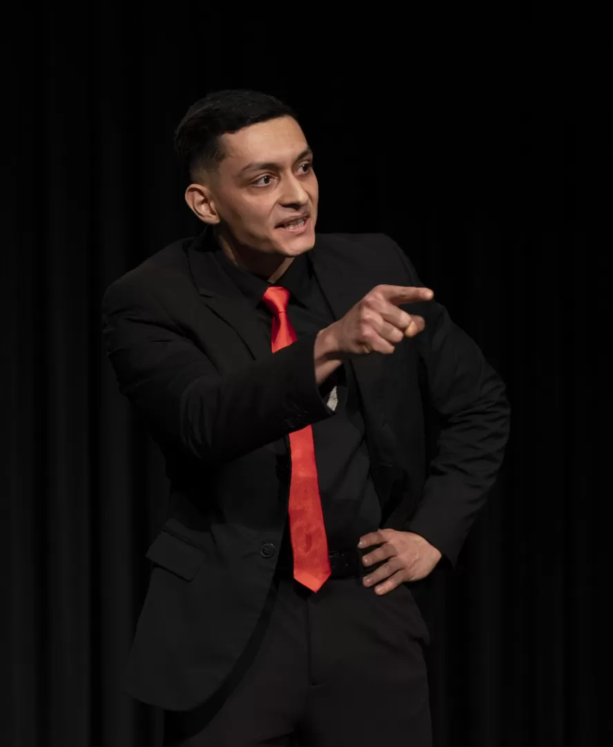 Ein Mann im schwarzen Anzug schaut wütend und zeigt mit einem Finger.