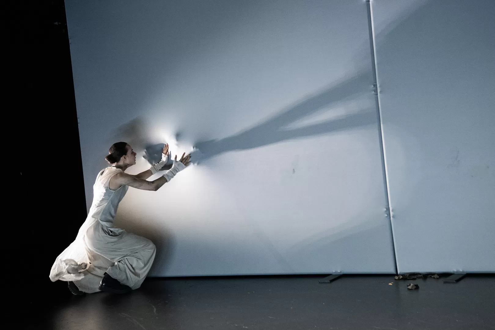 Darsteller*in legt ihre Hände an eine weiße Leinwand, dahinter scheint noch eine Person zu sein, die ebenfalls ihre Hände von der anderen Seite an die Leinwand legt.