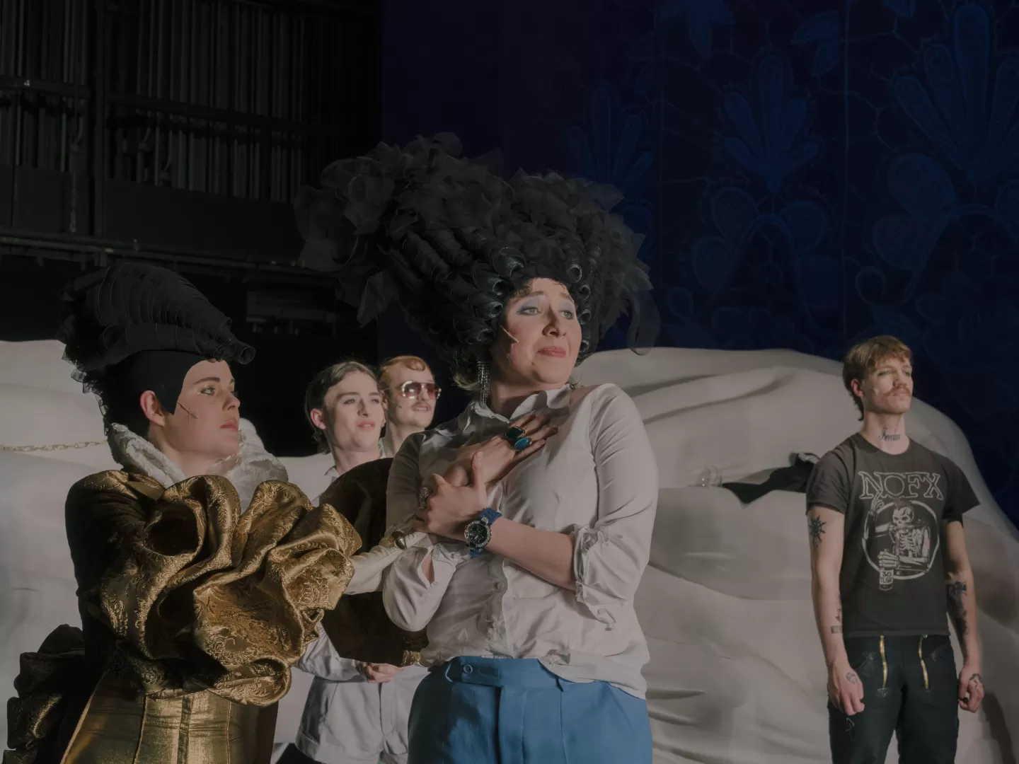 Szene aus Die Fledermaus, im Vordergrund eine Darstellerin, die mit großer Perücke ausgestattet ist und sehnsüchtig nach links blickt.