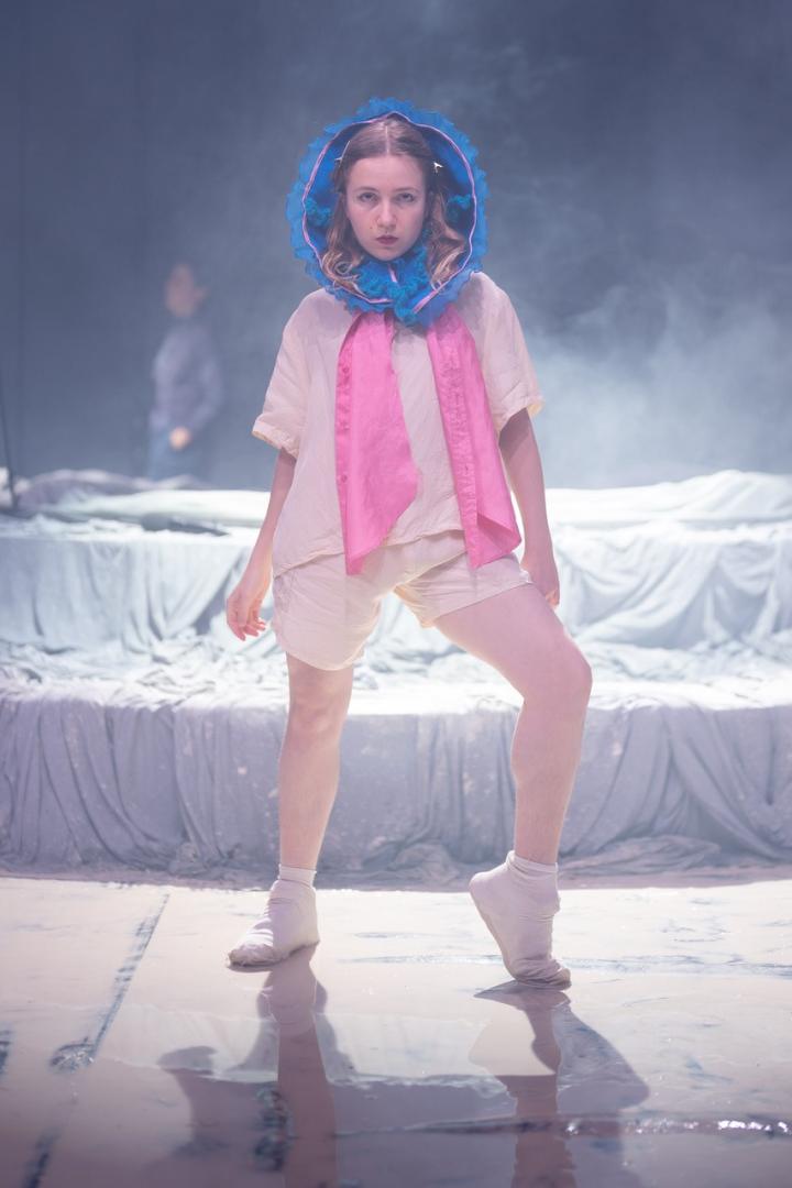 Darstellerin posiert in rosa Outfit auf der Bühne, um den Kopf eine blaue Kapuze gelegt.