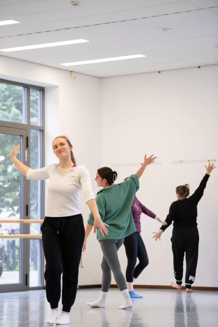 Vier Studierende bewegen sich im MA CoDE Studio, jeweils einen Arm schräg nach unten, und den anderen Arm schräg nach oben gestreckt.