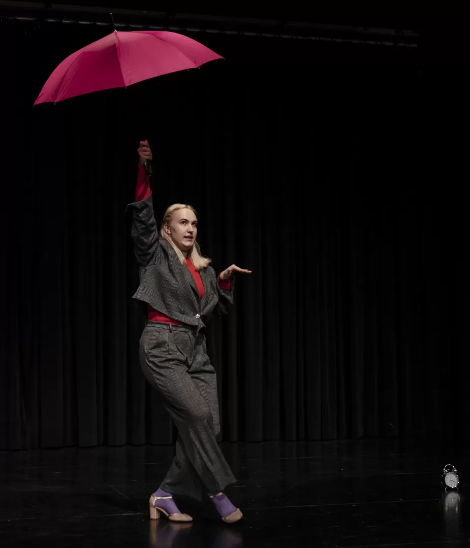 Eine Frau in einem grauen Anzug und einem rosa Regenschirm in der Hand