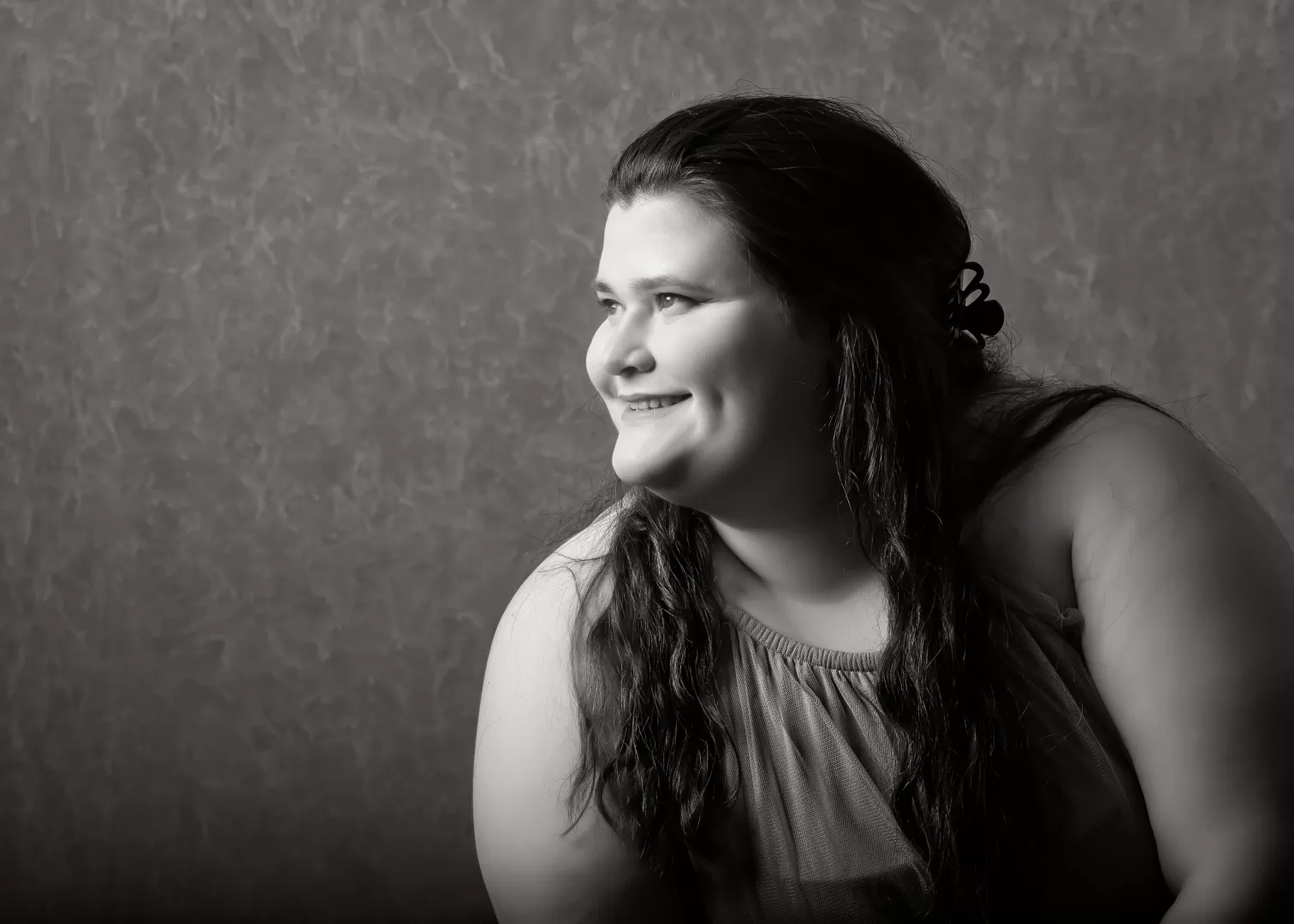 Ein horizontales Portraitfoto von Sophie-Charlotte Rees in schwarz-weiß. Sie ist in der rechten Bildhälfte und schaut lächelnd nach links. Sie hat dunkle, lange Haare, die vorderen Strähnen sind mit einer Klammer nach hinten gesteckt.