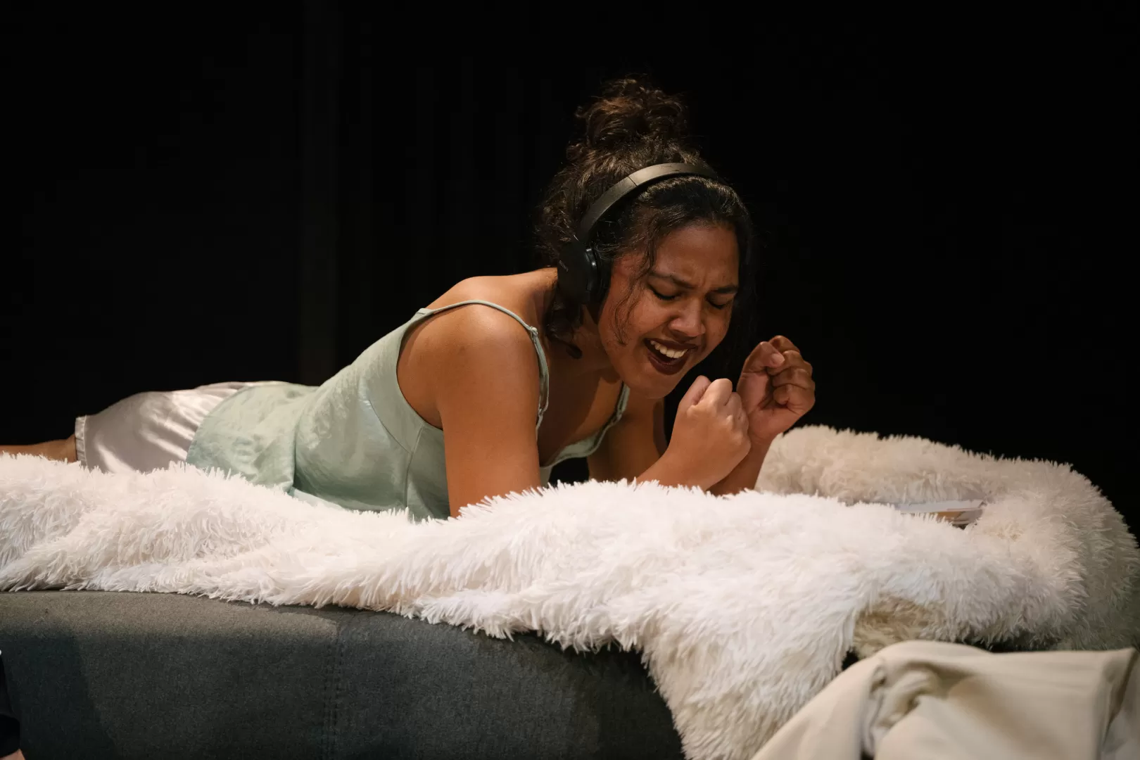 Frau liegt mit Kopfhörer auf einem Bett und singt.