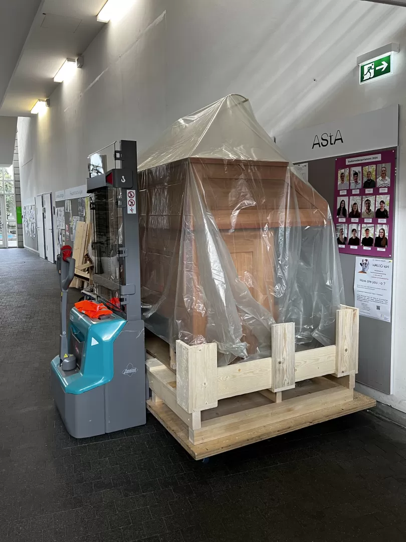 Der eingepackte Spieltisch steht vorm Schwarzen Brett im Foyer der Hochschule.