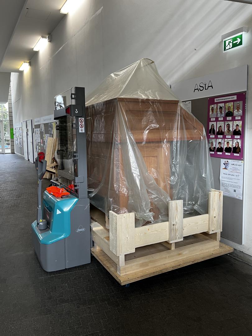 Der eingepackte Spieltisch steht vorm Schwarzen Brett im Foyer der Hochschule.