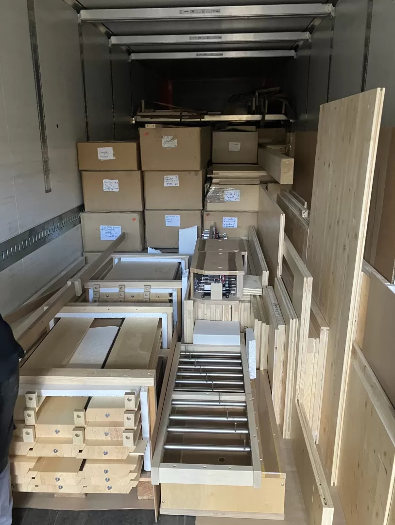 Der LKW ist fast voll geladen. Im Vordergrund liegen viele Holzplatten, im Hintergrund stapeln sich Kartons.