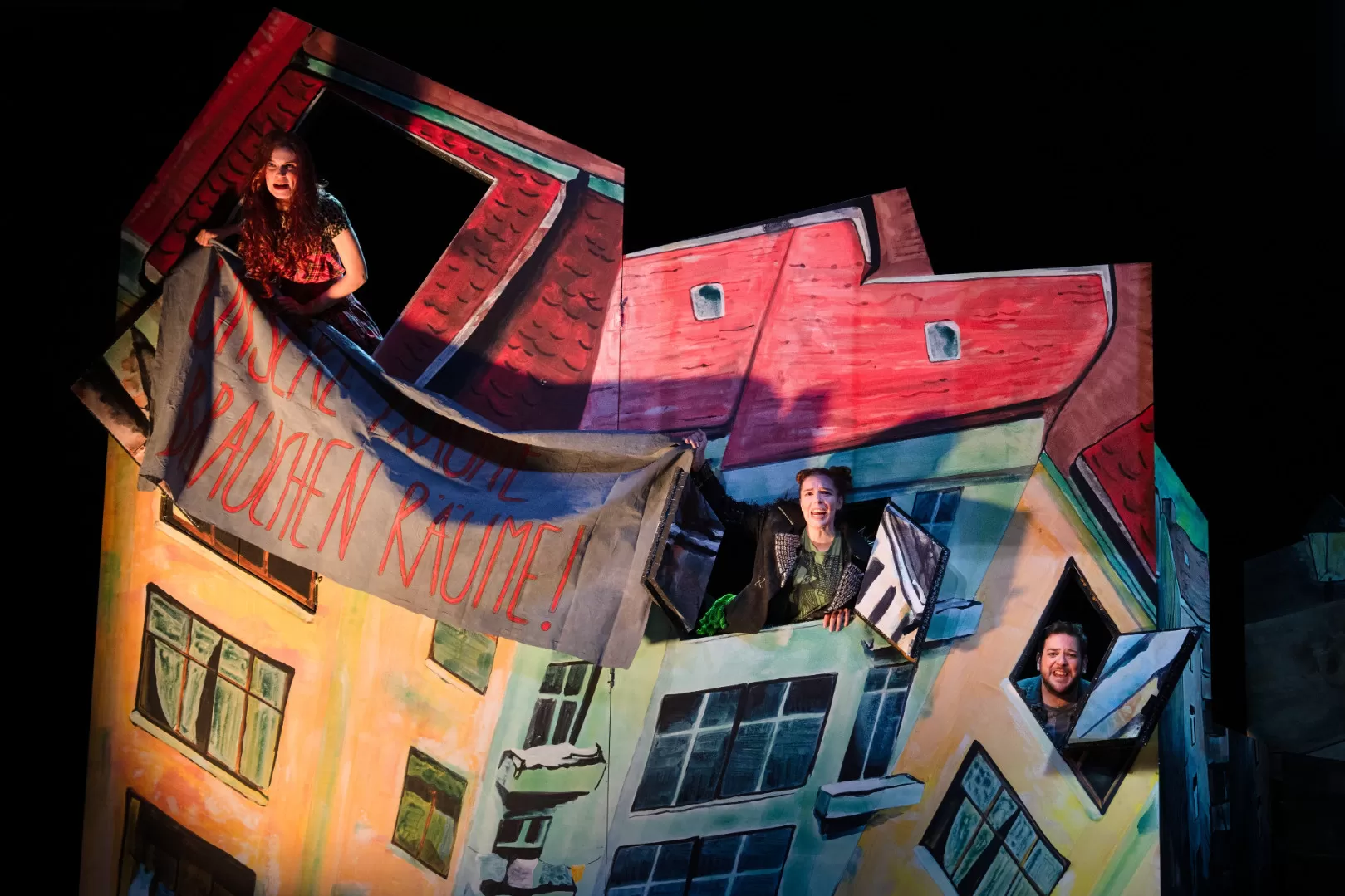 Zwei Menschen schauen aus einem Haus und halten einen Banner.