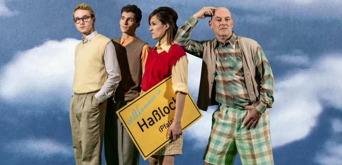 Vier Menschen stehen hinter blauem Hintegrunnd und halten ein Ortsschild