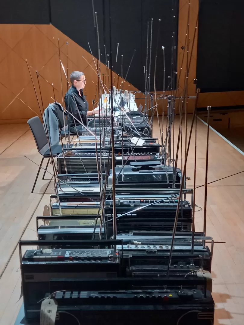 Auf einem langen Tisch stehen zahlreiche Radiogeräte, weiter hinten am Tisch sitzt Annette Schmucki von blablabor.