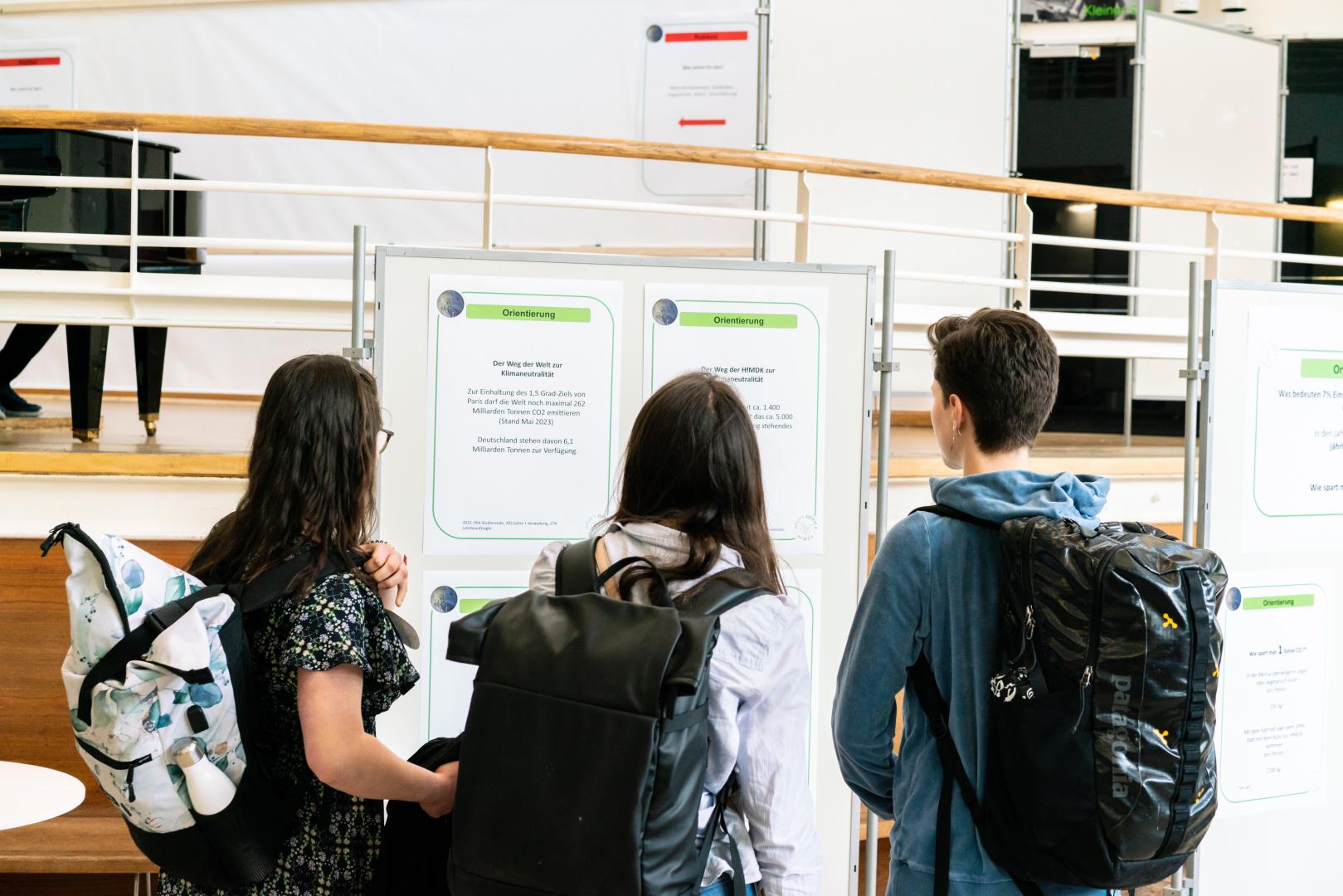Studierende schauen sich Aufsteller im Foyer an, an denen Infos zum Thema Nachhaltigkeit hängen.