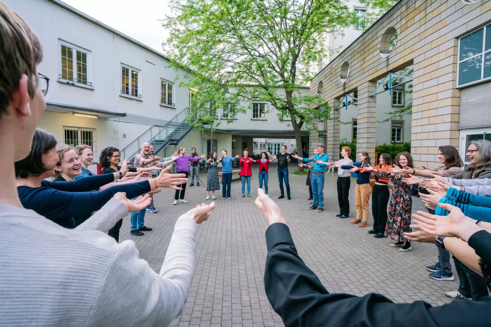 Im Innenhof stehen Menschen in einem Kreis und strecken die Hände aus in die Richtung Mitte.