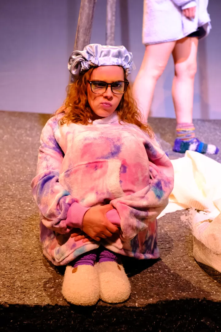 Eine Frau mit Birlle und Locken sitzt mit den Knien in der Hand und schmollt