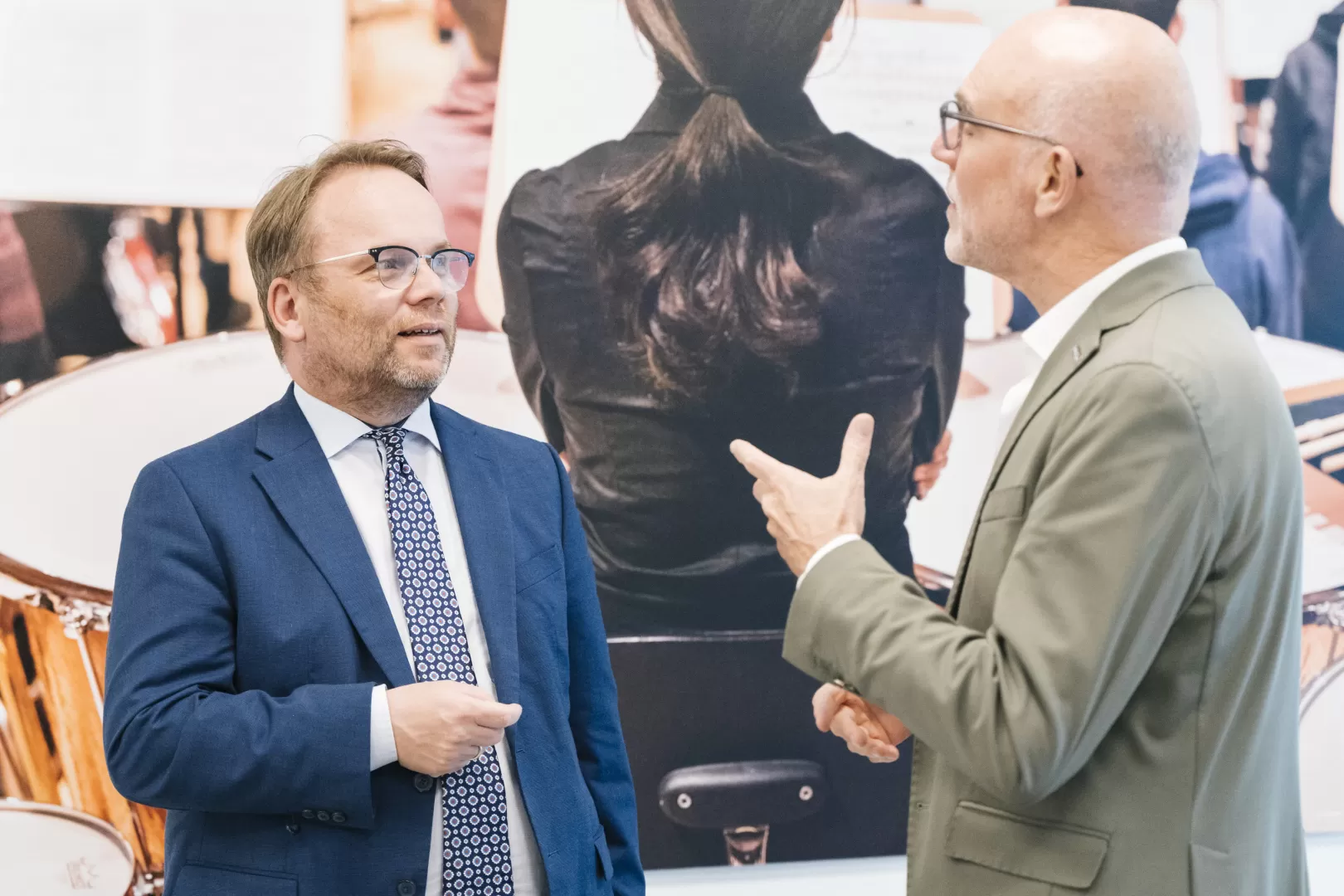 Timon Gremmels und Prof. Elmar Fulda, beide tragen Anzug, unterhalten sich vor dem großen Bild einer Musikerin