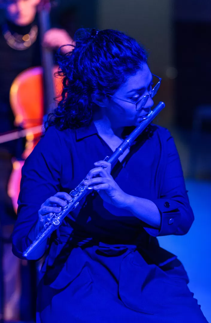 Eine Flötistin spielt auf ihrer Querflöte, umgeben von blauem Licht.