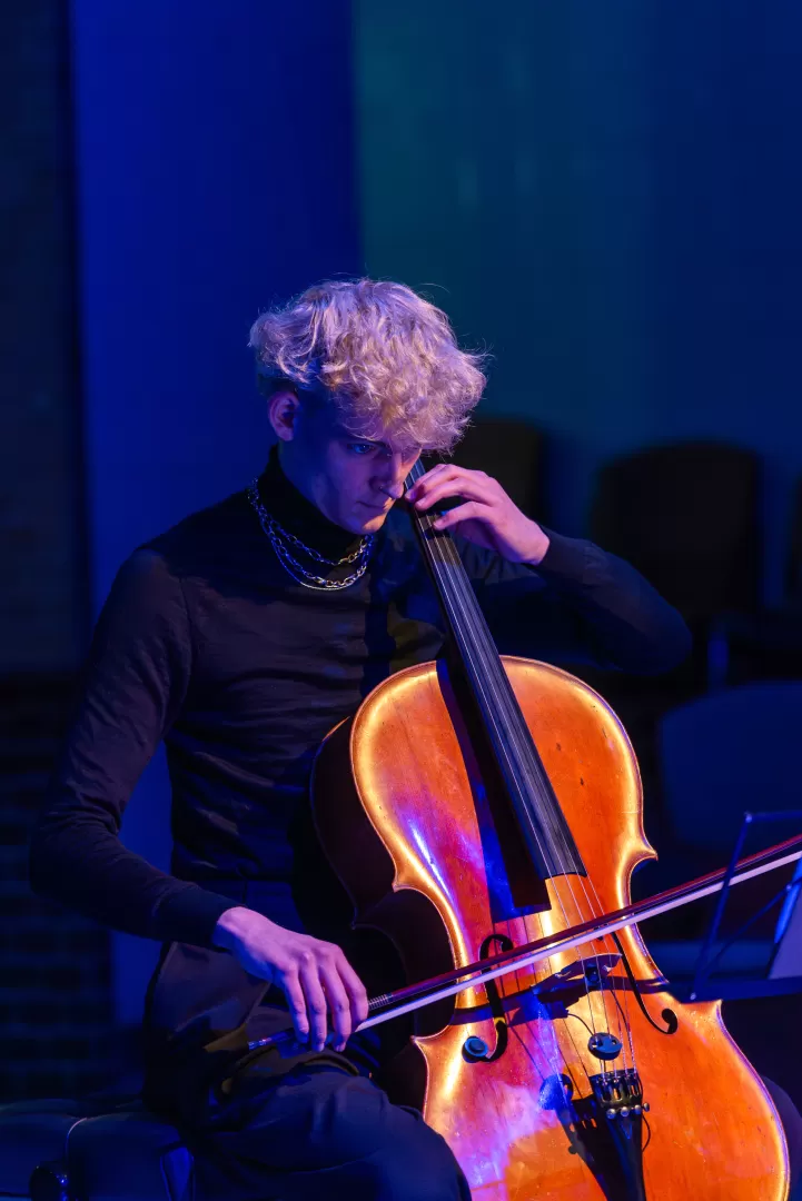 Ein Student spielt Cello. Um ihn herum ist blaues Licht.