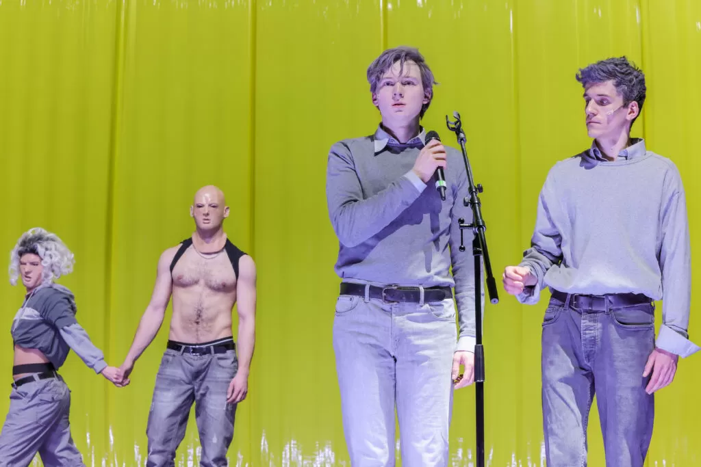 Vier Menschen stehen vor einer gelben Wand, sie sind grau angezogen.