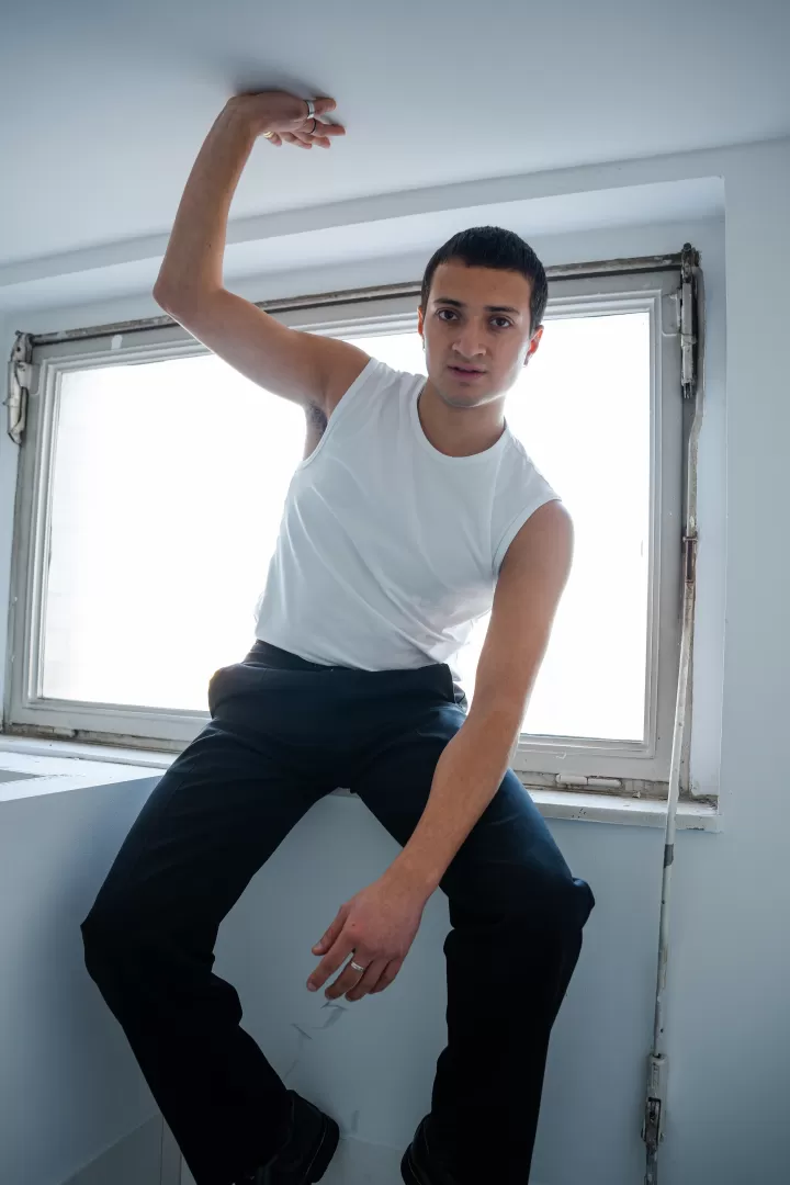 Pablo Weller de la Torre sitzt in einem weißen Tanktop und schwarzer Hose auf einer weiß gefließten Fensterbank.