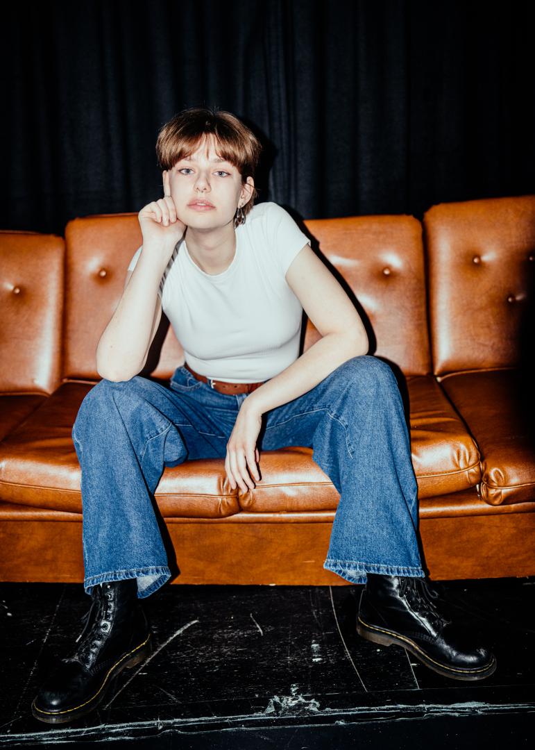 Totale Paula Marie Schulze, weißes T-shirt, blaue Jeans, im Hintergrund eine braune Ledercouch