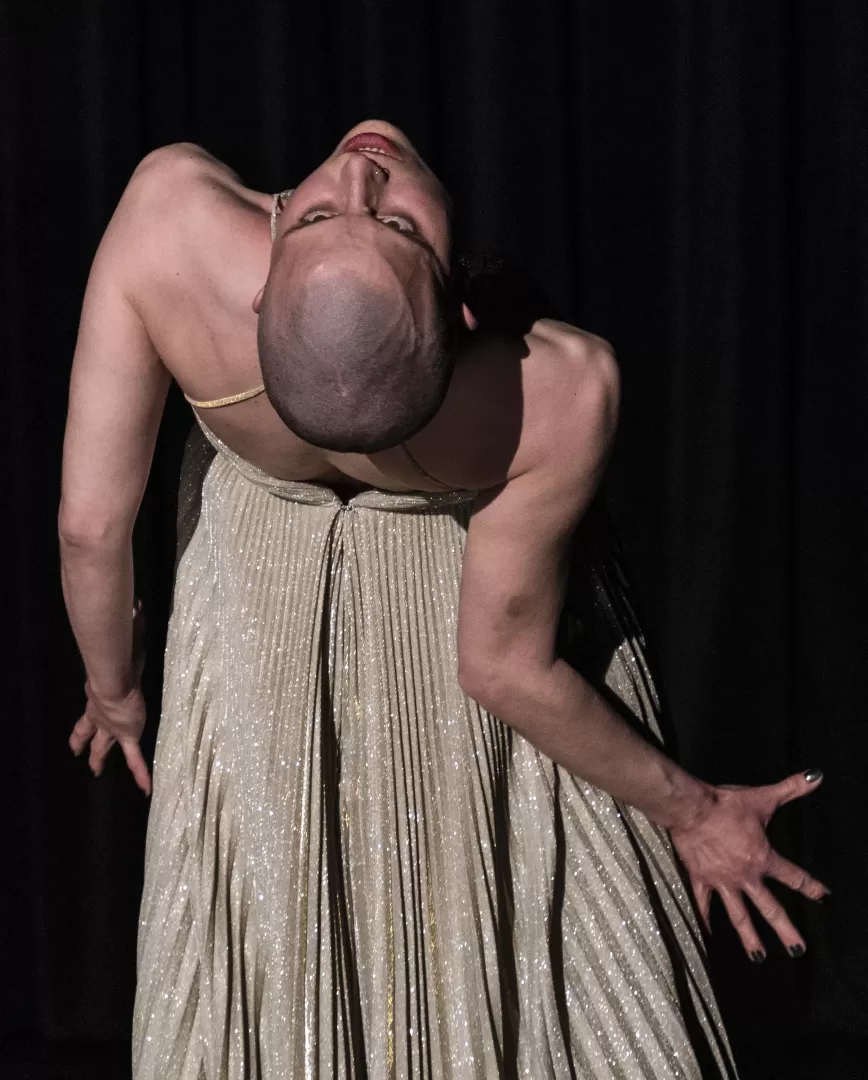 Lisa steht mit dem Rücken zum Publikum und beugt sich angespannt nach hinten. Sie trägt ein silbernes, glitzerndes Kleid.