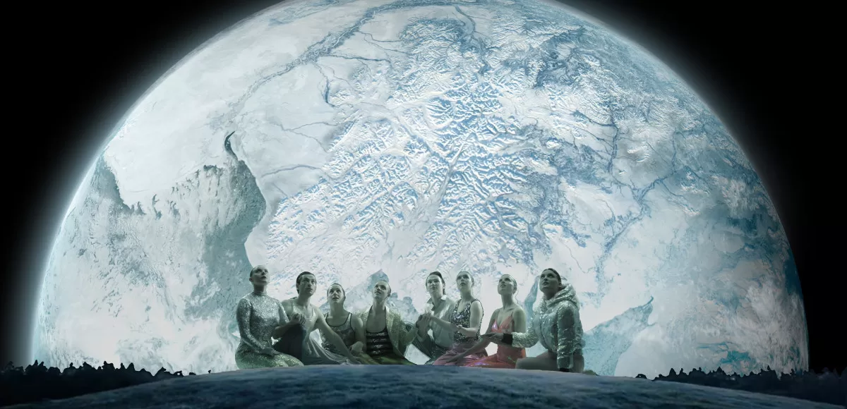 Acht Menschen in rosa und Silber gekleidet sitzen vor einem großen projizierten Mond