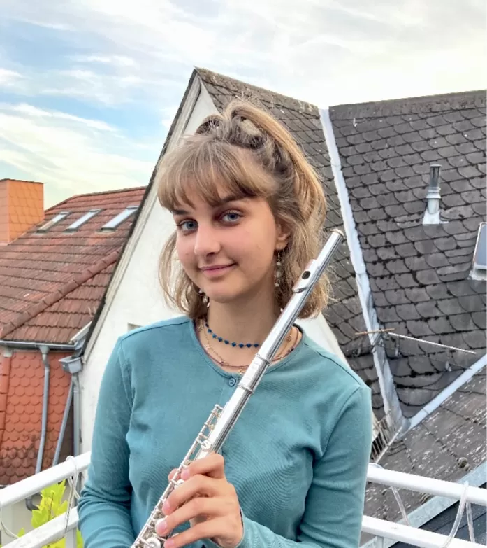 Amelie Schröder steht auf einem Balkon und hält ihre Querflöte in den Händen.