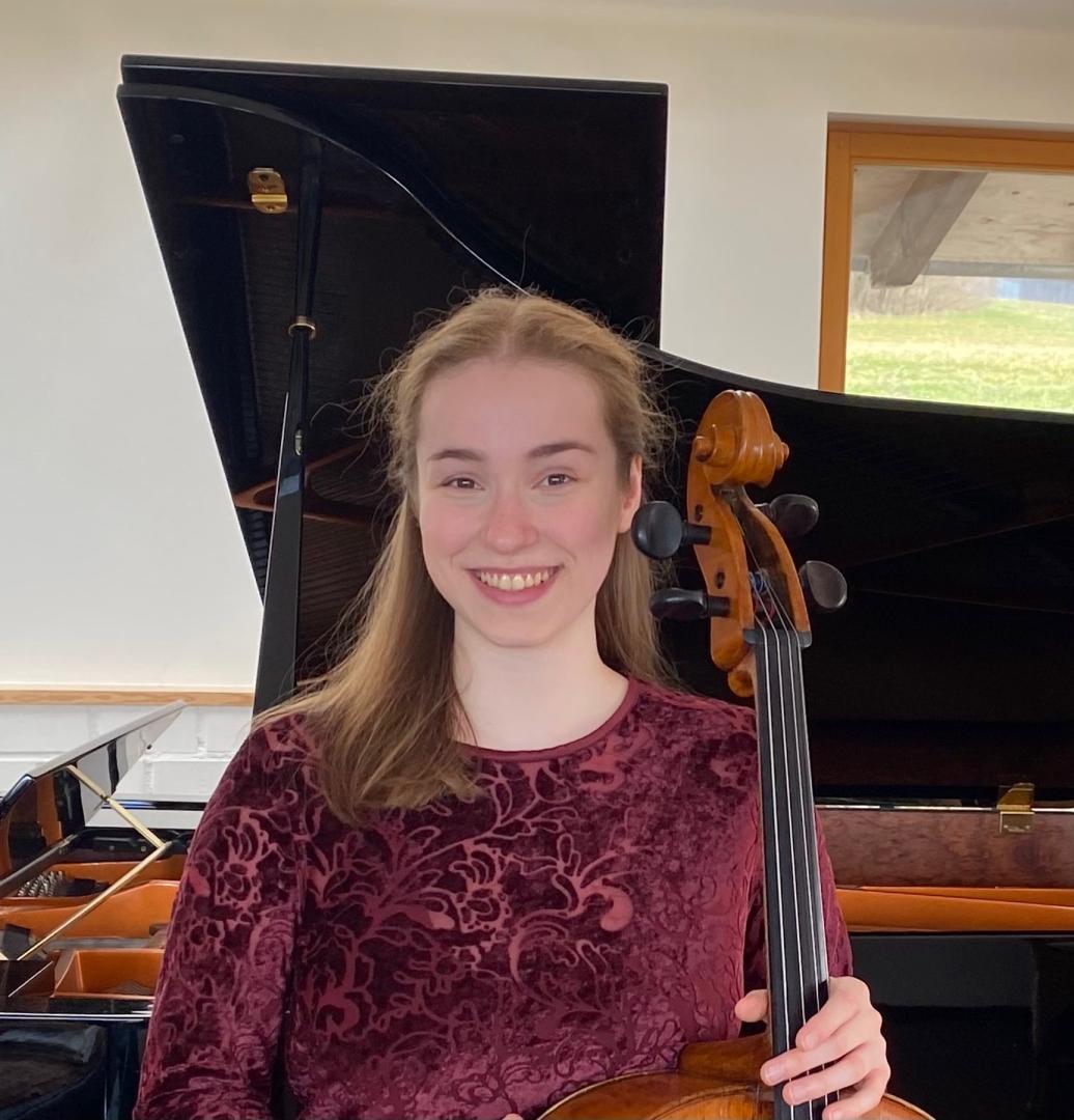 Clara Stümke lächelt in die Kamera und hält ihr Cello in der Hand.
