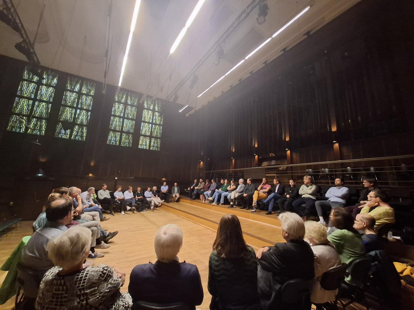 Gruppe sitzt in einem großen Stuhlkreis im Großen Saal