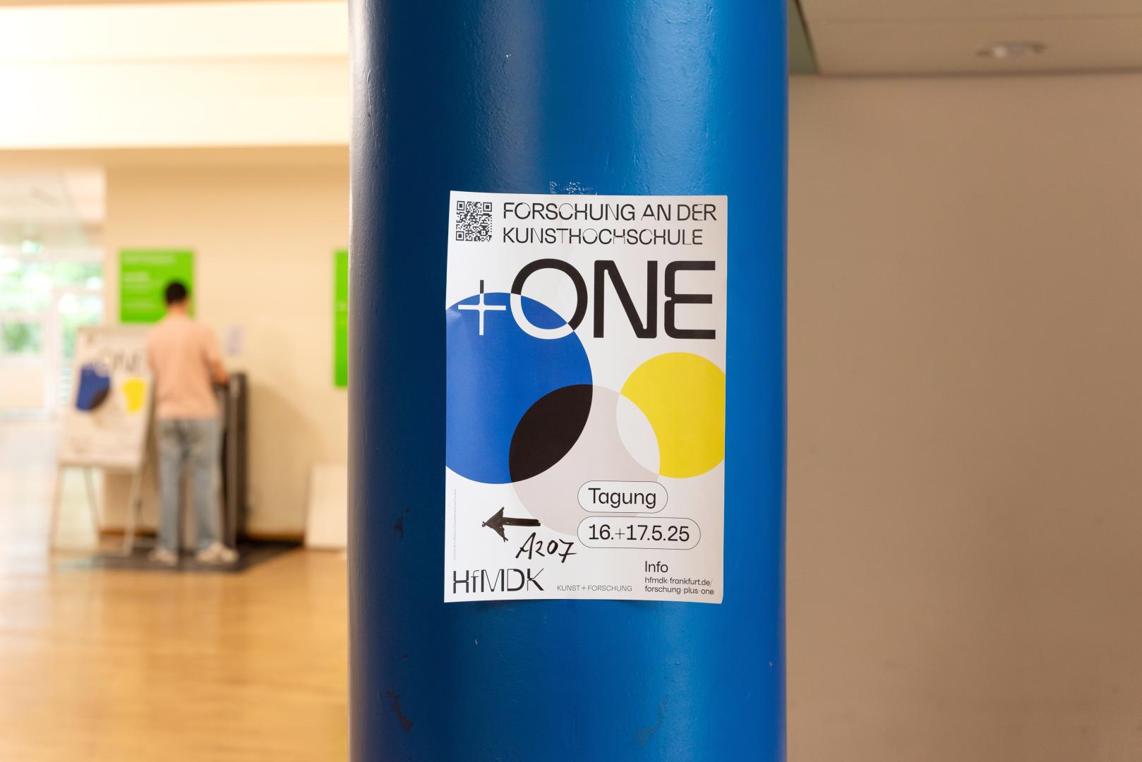 Eine Säule, in der das Plakat der Tagung "Forschung an der Kunsthochschule +ONE" angebracht ist.