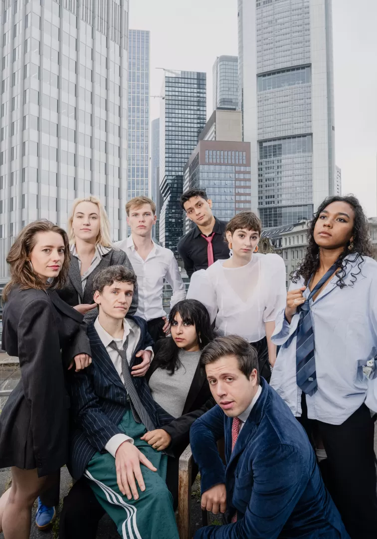 Neun Menschen stehen lachend vor einer Skyline 