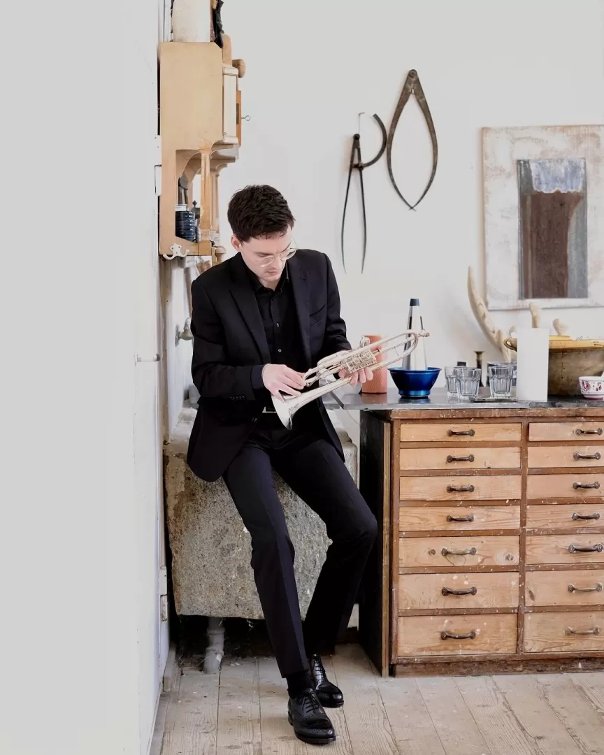Trompeter Sebastian Kellner steht in einem Atelier mit seinem Instrument in der Hand