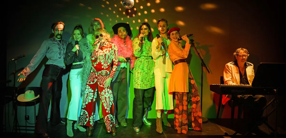 Acht Leute in bunter Kleidung singen auf einer Bühne