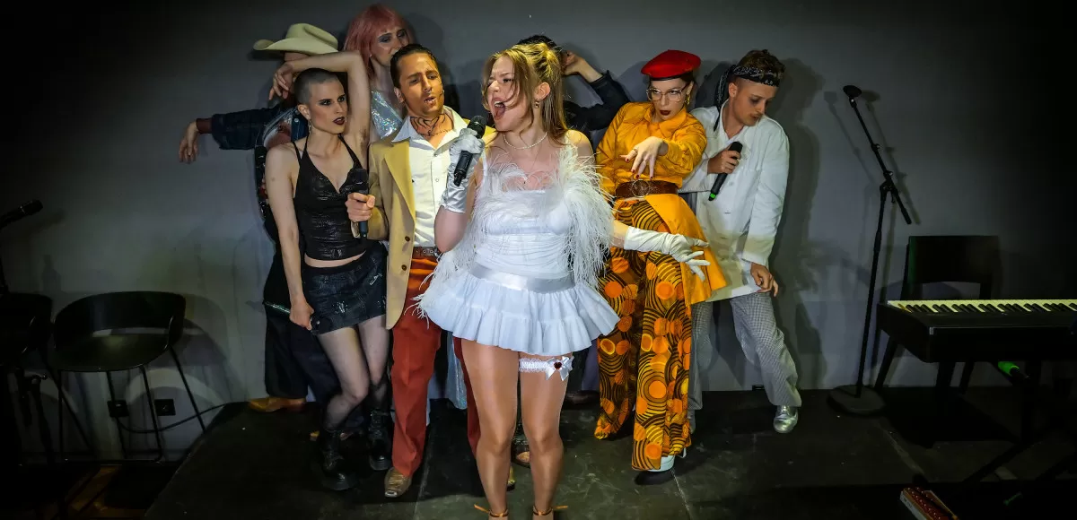 Acht Leute in bunter Kleidung singen auf einer Bühne