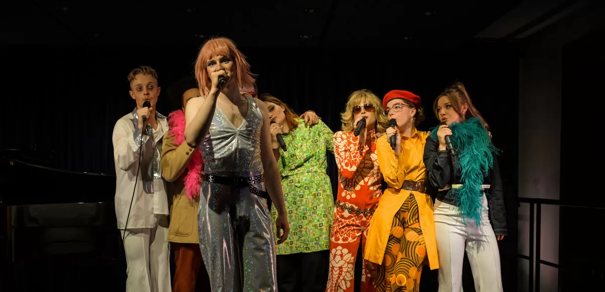 Acht Leute in bunter Kleidung singen auf einer Bühne