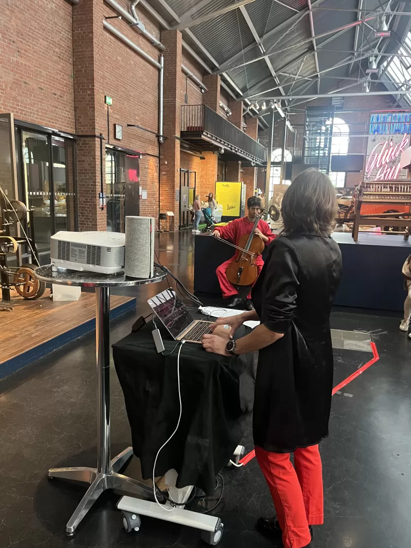 Rot-schwarz gekleidete Menschen musizieren im Industriemuseum. Im Vordergrund steht eine Studentin am Laptop.