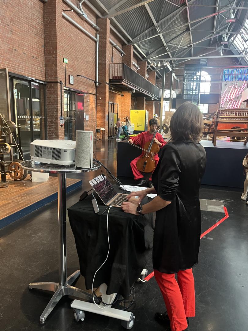 Rot-schwarz gekleidete Menschen musizieren im Industriemuseum. Im Vordergrund steht eine Studentin am Laptop.