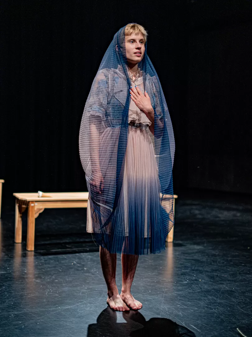 Lisa Freiberger hat den Rock ihres Kleides als Schleier über den Kopf gezogen und hält eine Hand an die Brust.