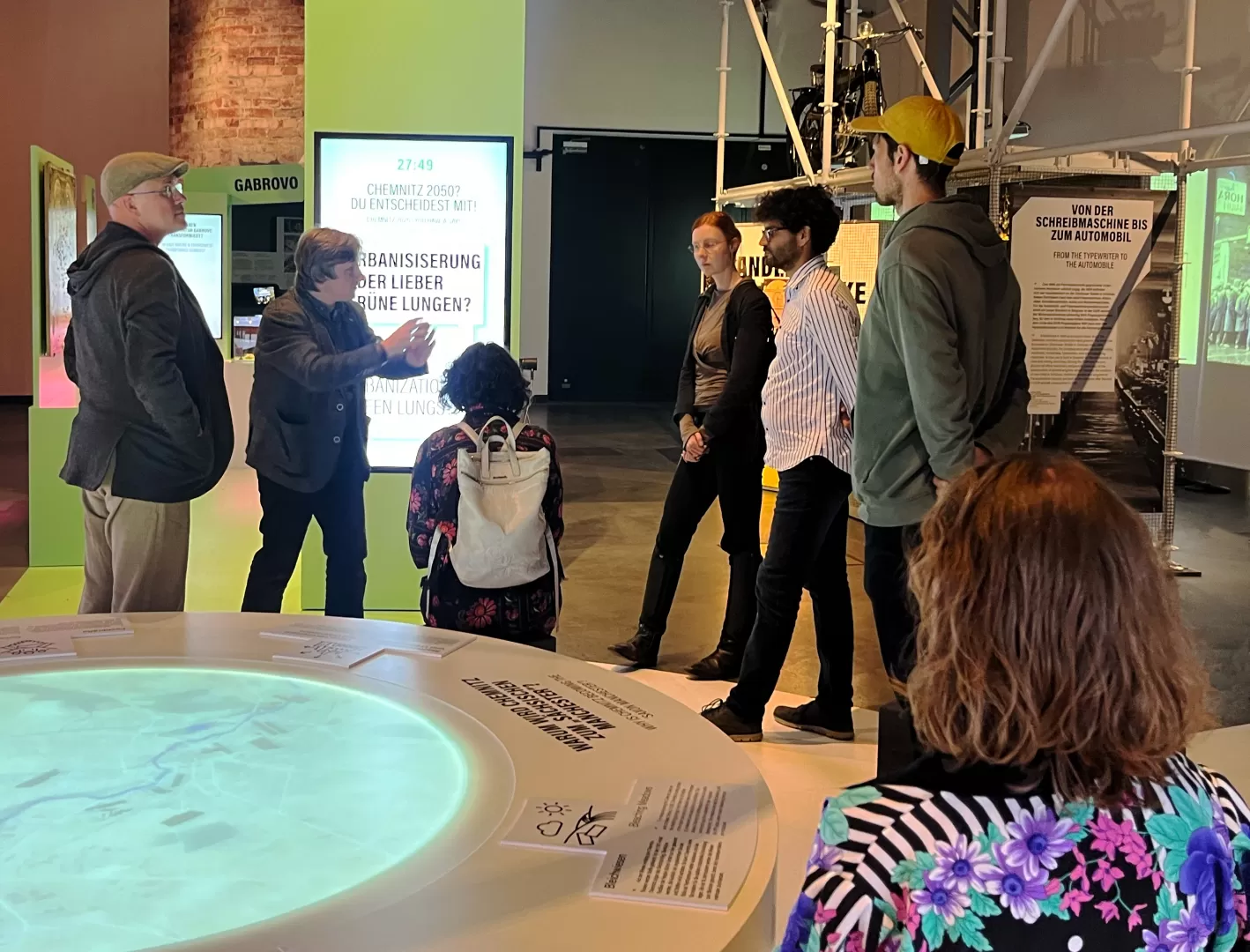 Mehrere Menschen stehen in einem Museum, einer von ihnen scheint den anderen etwas zu erklären.