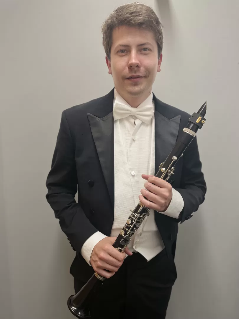 Zoltán Nagy trägt einen schwarzen Anzug, hält eine Klarinette in der Hand und blickt in die Kamera.