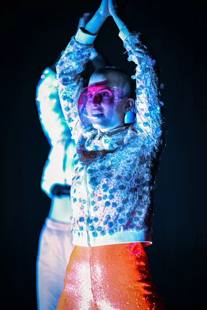 Lisa hat die Hände über dem Kopf zusammengeschlagen und blickt schräg nach vorne. Sie trägt ein Visier.