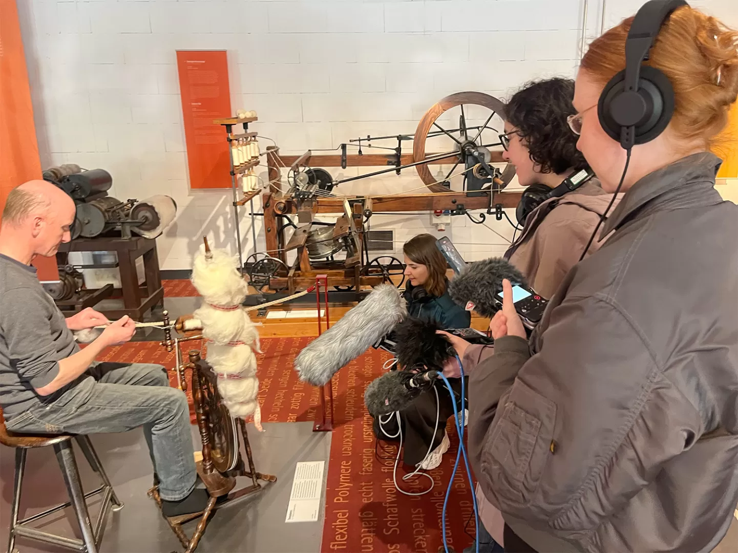 Ein Mann sitzt an einem Spinnrad. Mehrere Studierenden nehmen die Geräusche mit Mikrofonen und Kameras auf.