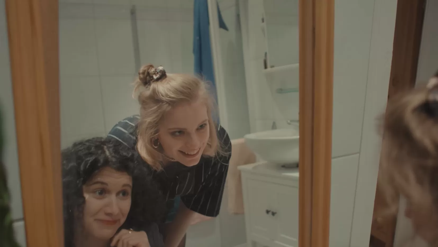 Zwei junge Frauen lächelnd vor einem großen Badezimmerspiegel.