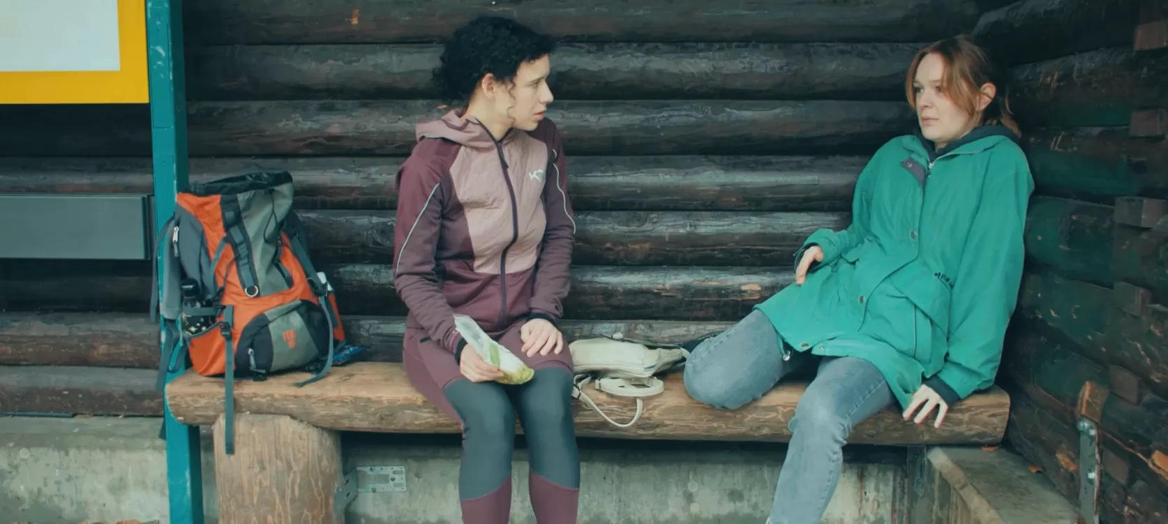 Zwei Frauen an einer Bushaltestelle in Wanderbekleidung.