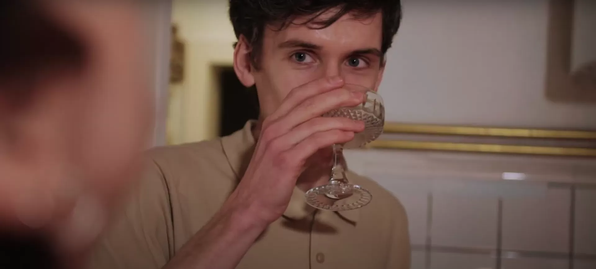 Ein Mann trinkt in einer Küche aus einem Cocktailglas.