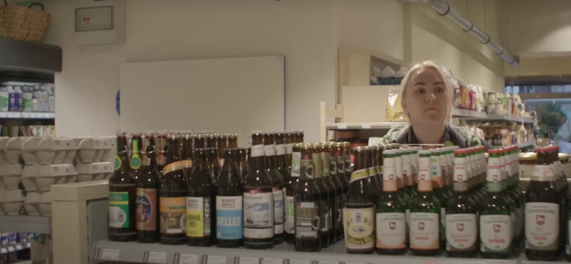 Eine Mitarbeiterin schaut in einem Supermarkt prüfend über ein Regal hinweg.