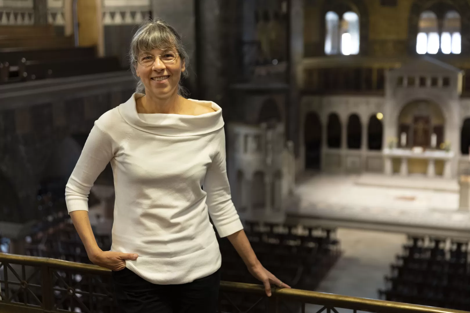 Susanne Rohn trägt ein schickes, weißes Oberteil und hält sich an der Emporenbrüstung fest. Blick in Kirchenraum