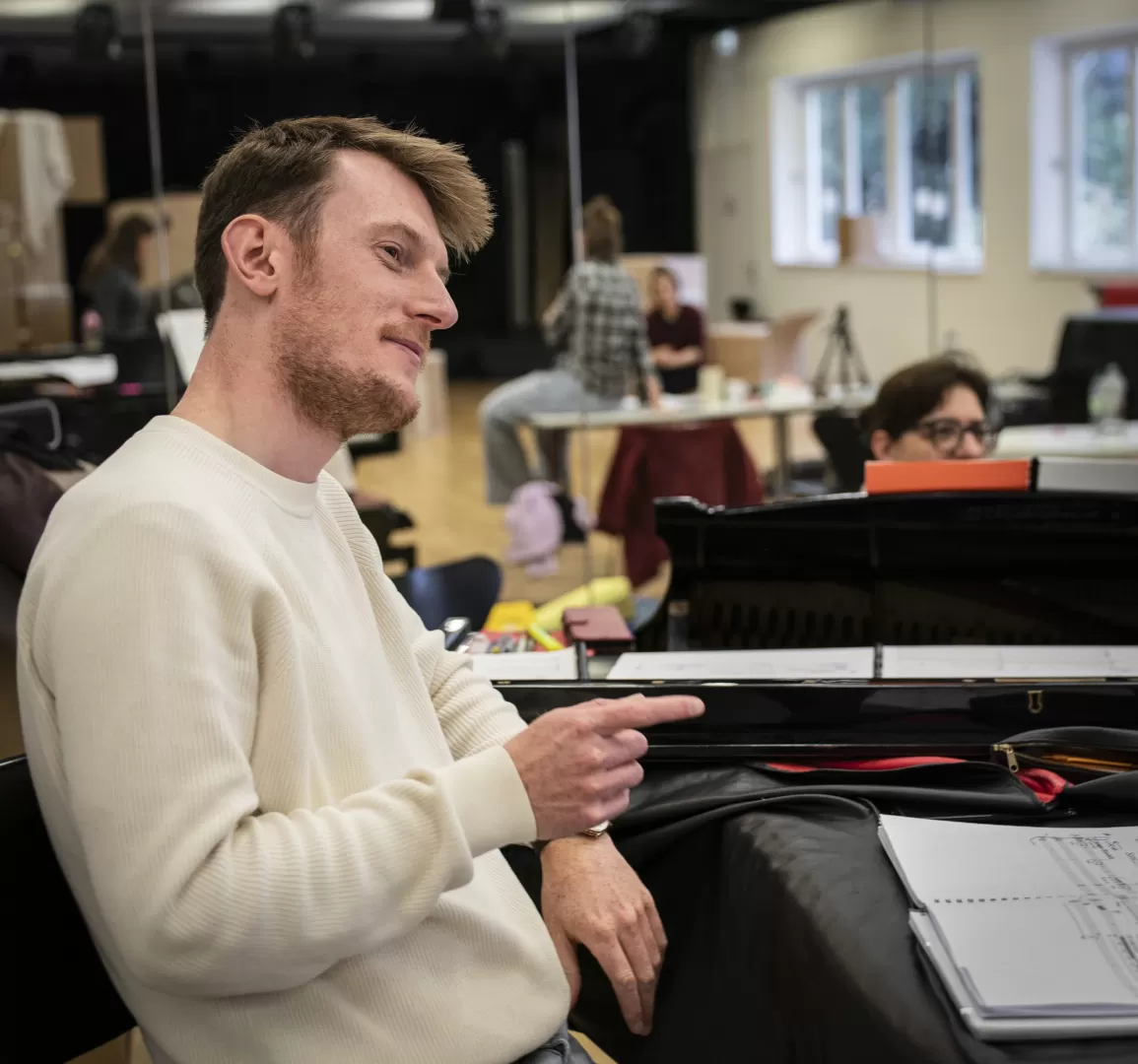 Ein Mann steht an einem Klavier und spricht mit jemandem